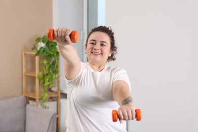 Photo of Plus size woman with dumbbells training at home