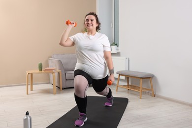 Photo of Plus size woman with dumbbells training at home