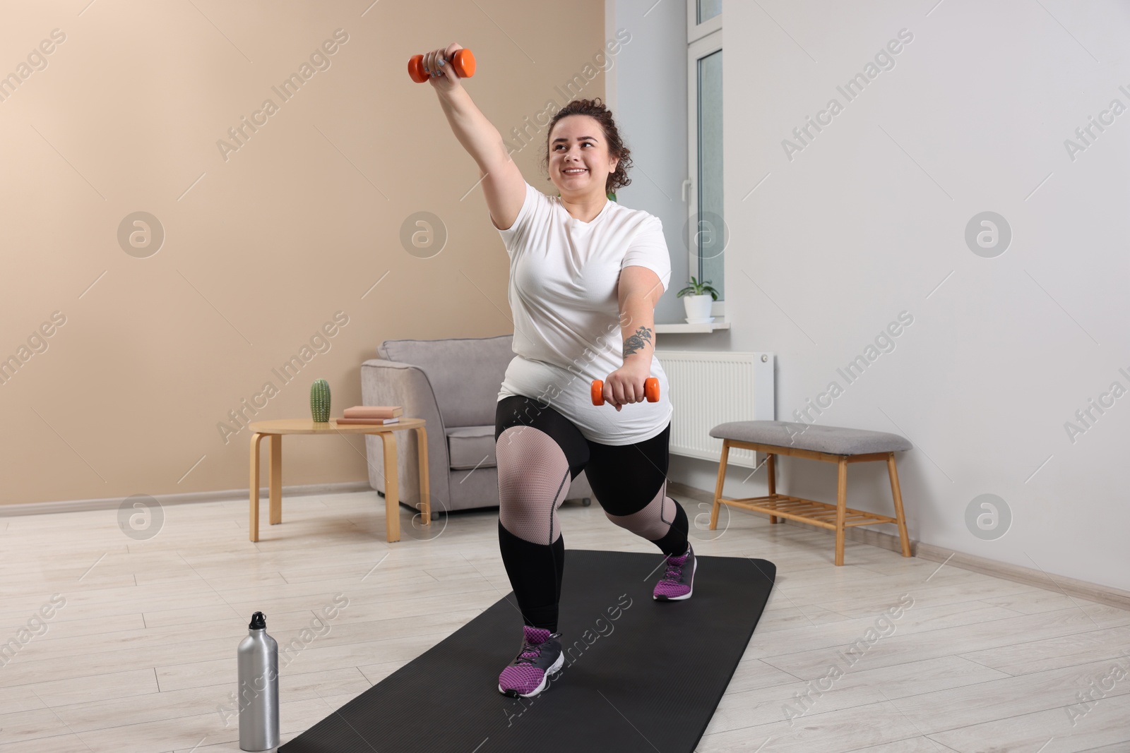 Photo of Plus size woman with dumbbells training at home