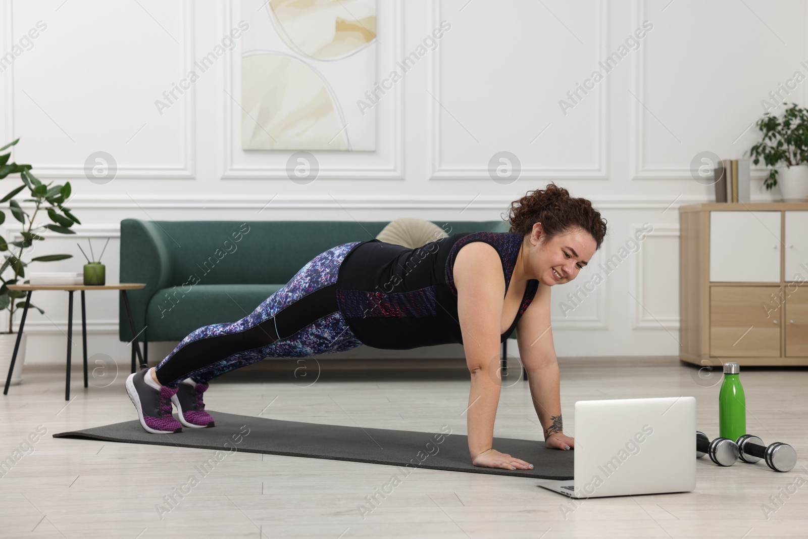 Photo of Plus size woman having fitness training with online coach via laptop at home