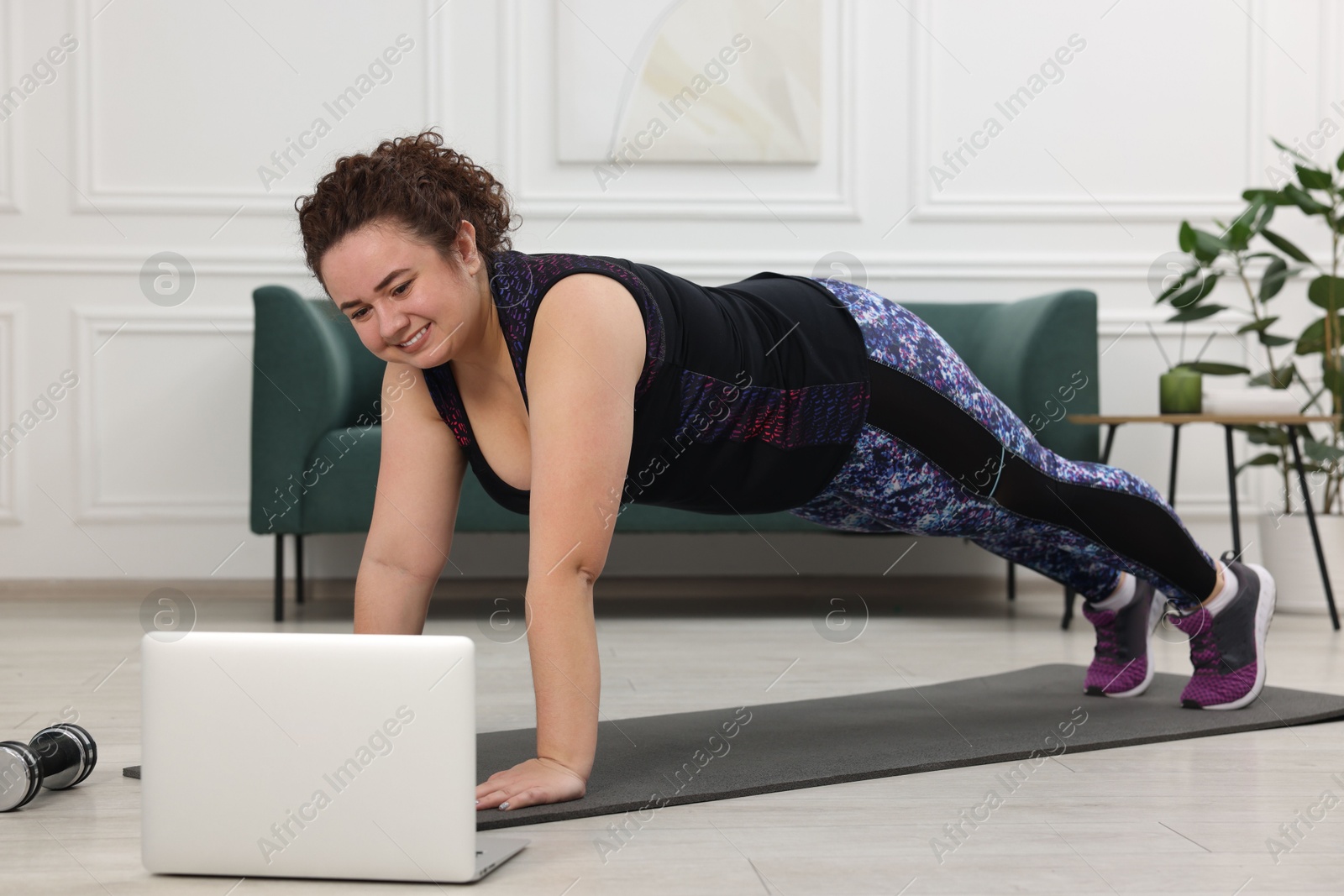 Photo of Plus size woman having fitness training with online coach via laptop at home