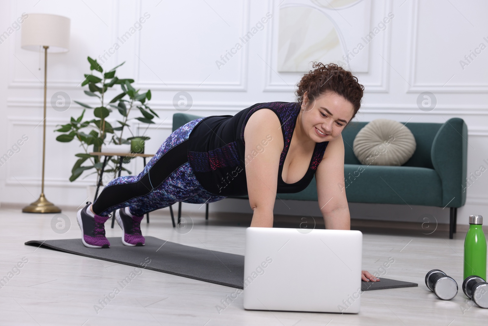 Photo of Plus size woman having fitness training with online coach via laptop at home