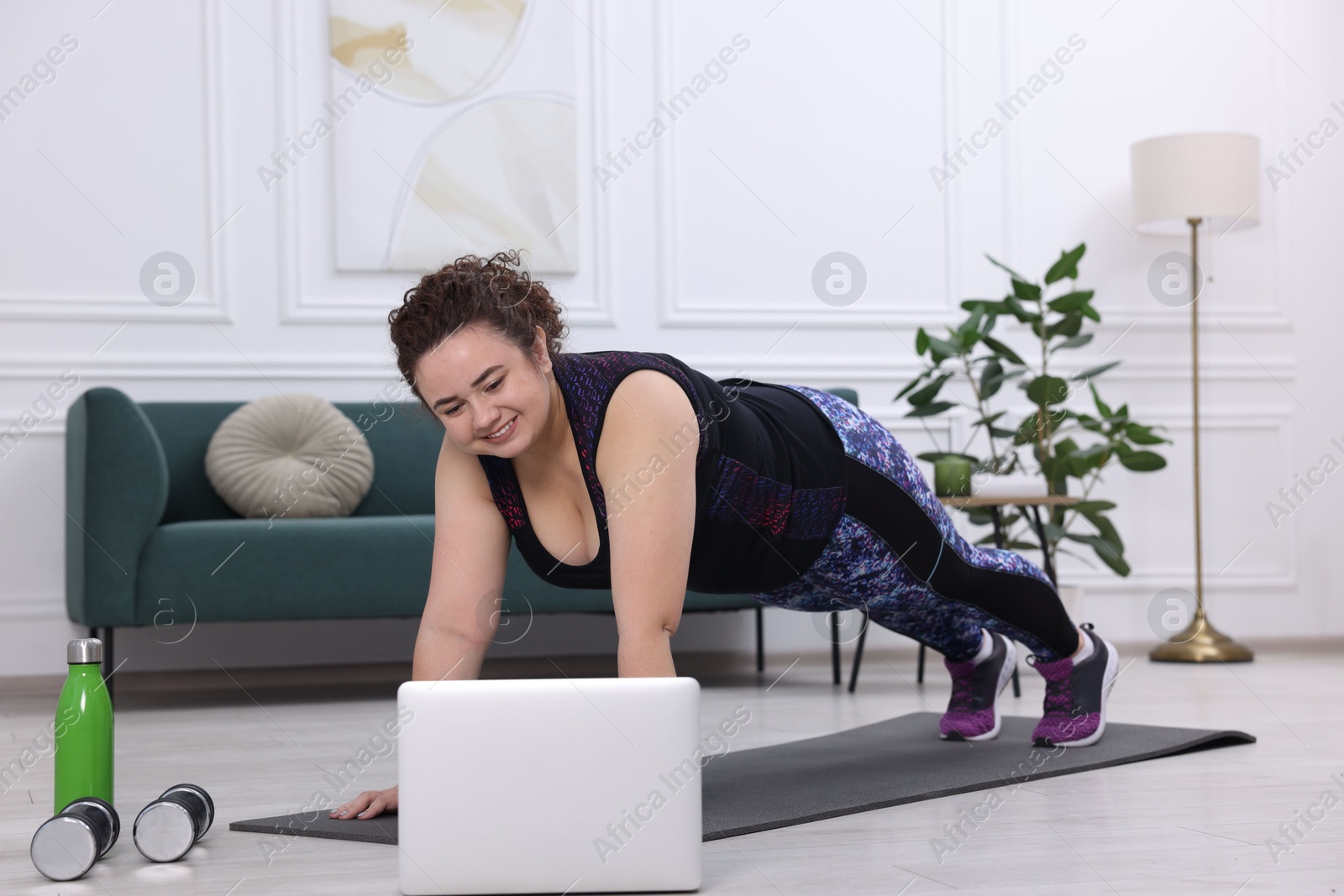 Photo of Plus size woman having fitness training with online coach via laptop at home