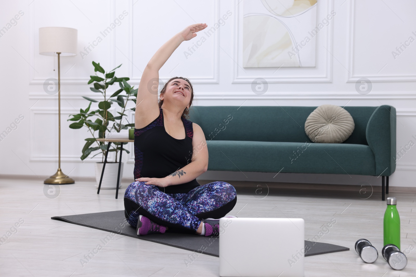 Photo of Plus size woman having fitness training with online coach via laptop at home