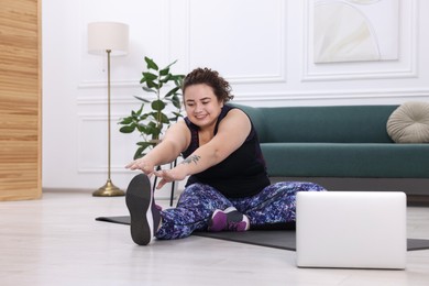 Photo of Plus size woman having fitness training with online coach via laptop at home