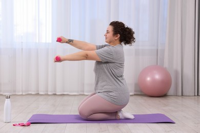 Photo of Plus size woman with dumbbells training at home