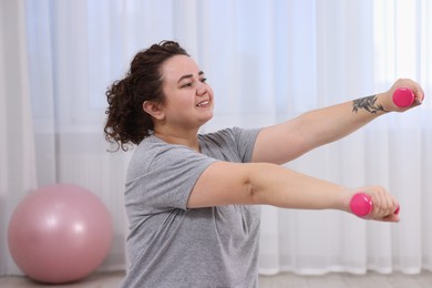 Photo of Plus size woman with dumbbells training at home