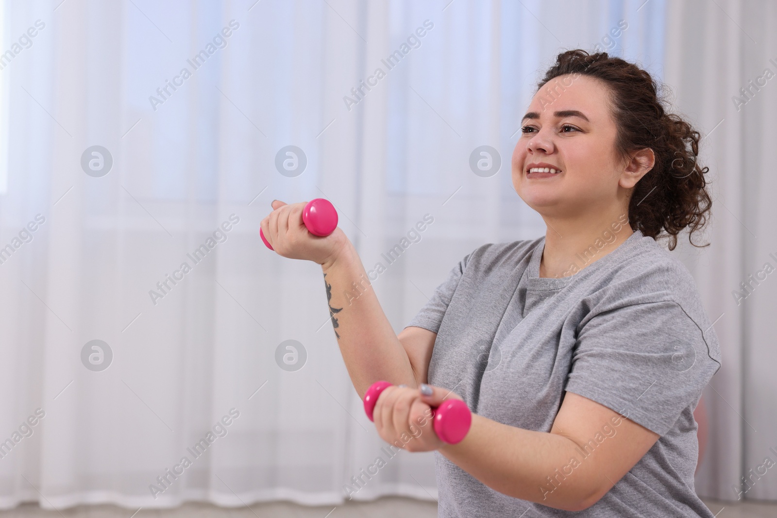 Photo of Plus size woman with dumbbells training at home