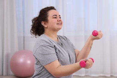 Photo of Plus size woman with dumbbells training at home