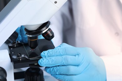 Photo of Scientist examining sample on slide under microscope, closeup