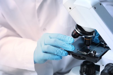 Scientist examining sample on slide under microscope, closeup