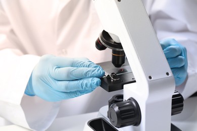 Photo of Scientist examining sample on slide under microscope at table, closeup