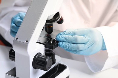 Scientist examining sample on slide under microscope at table, closeup