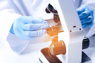 Scientist examining sample on slide under microscope at table, closeup