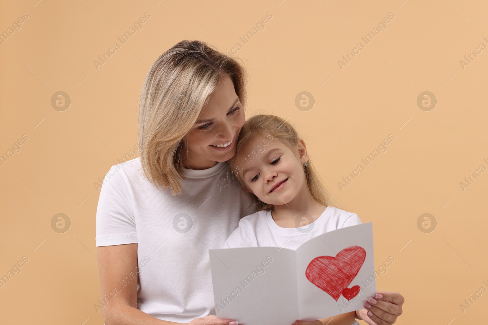 Photo of Happy woman with her daughter and greeting card on beige background. Mother's Day celebration