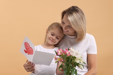 Photo of Happy woman with her daughter, bouquet of alstroemeria flowers and greeting card on beige background. Mother's Day celebration