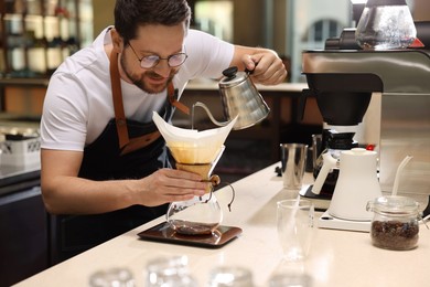 Photo of Barista brewing coffee in glass coffeemaker with paper filter at table in cafe