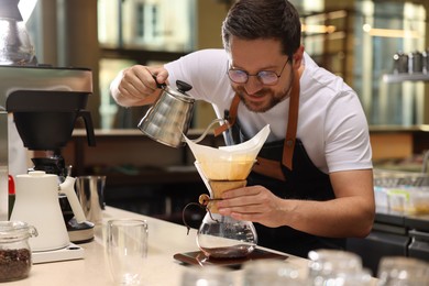 Barista brewing coffee in glass coffeemaker with paper filter at table in cafe