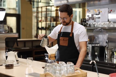 Photo of Barista brewing coffee in glass coffeemaker with paper filter at table in cafe