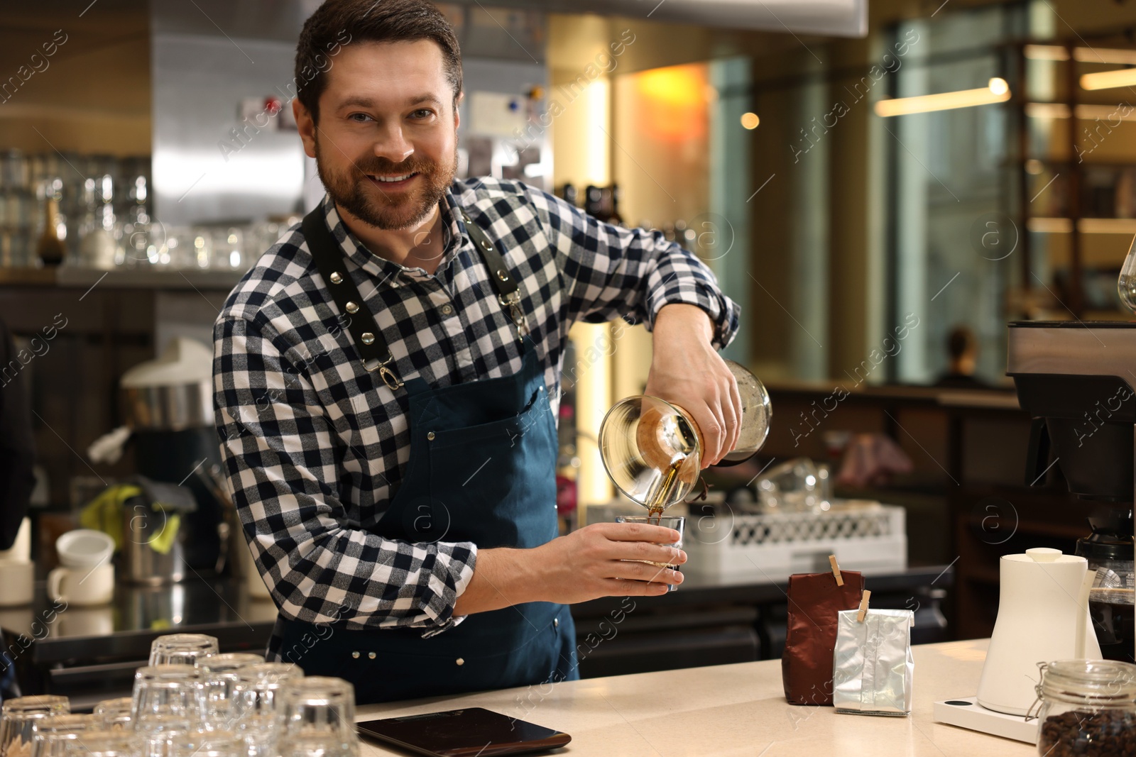 Photo of Barista pouring coffee from glass coffeemaker into cup at table in cafe