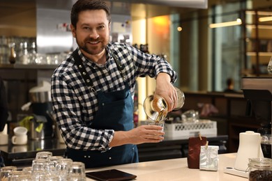 Photo of Barista pouring coffee from glass coffeemaker into cup at table in cafe