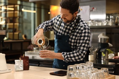 Barista pouring coffee from glass coffeemaker into cup at table in cafe