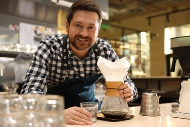 Photo of Barista making coffee with glass coffeemaker at table in cafe