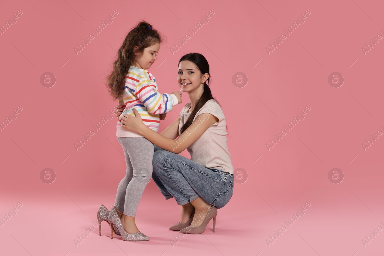 Photo of Cute little girl with lip gloss and her sister on pink background