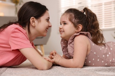 Photo of Cute little girl and her sister on rug at home