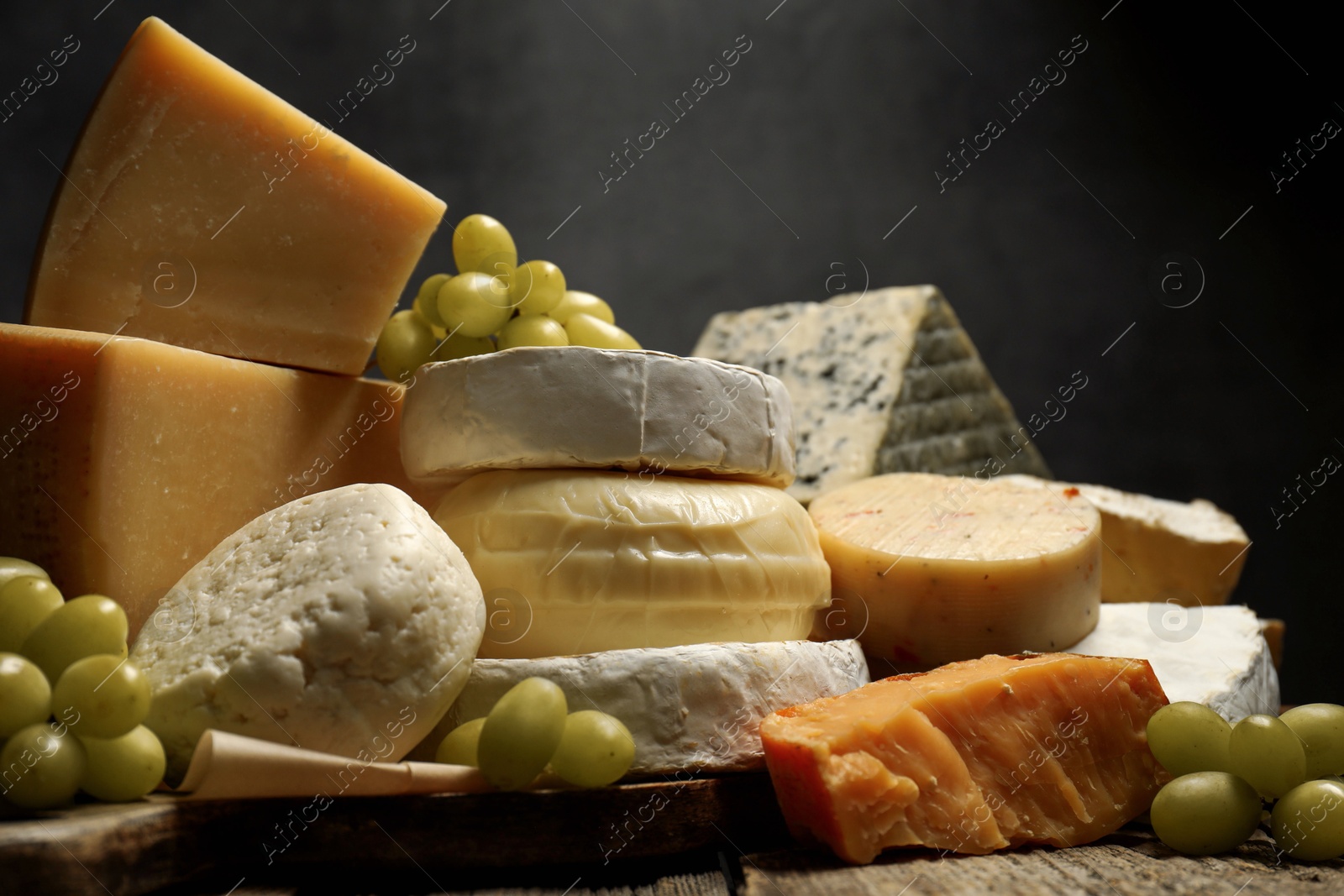 Photo of Different types of cheese and grapes on wooden table against dark background, closeup