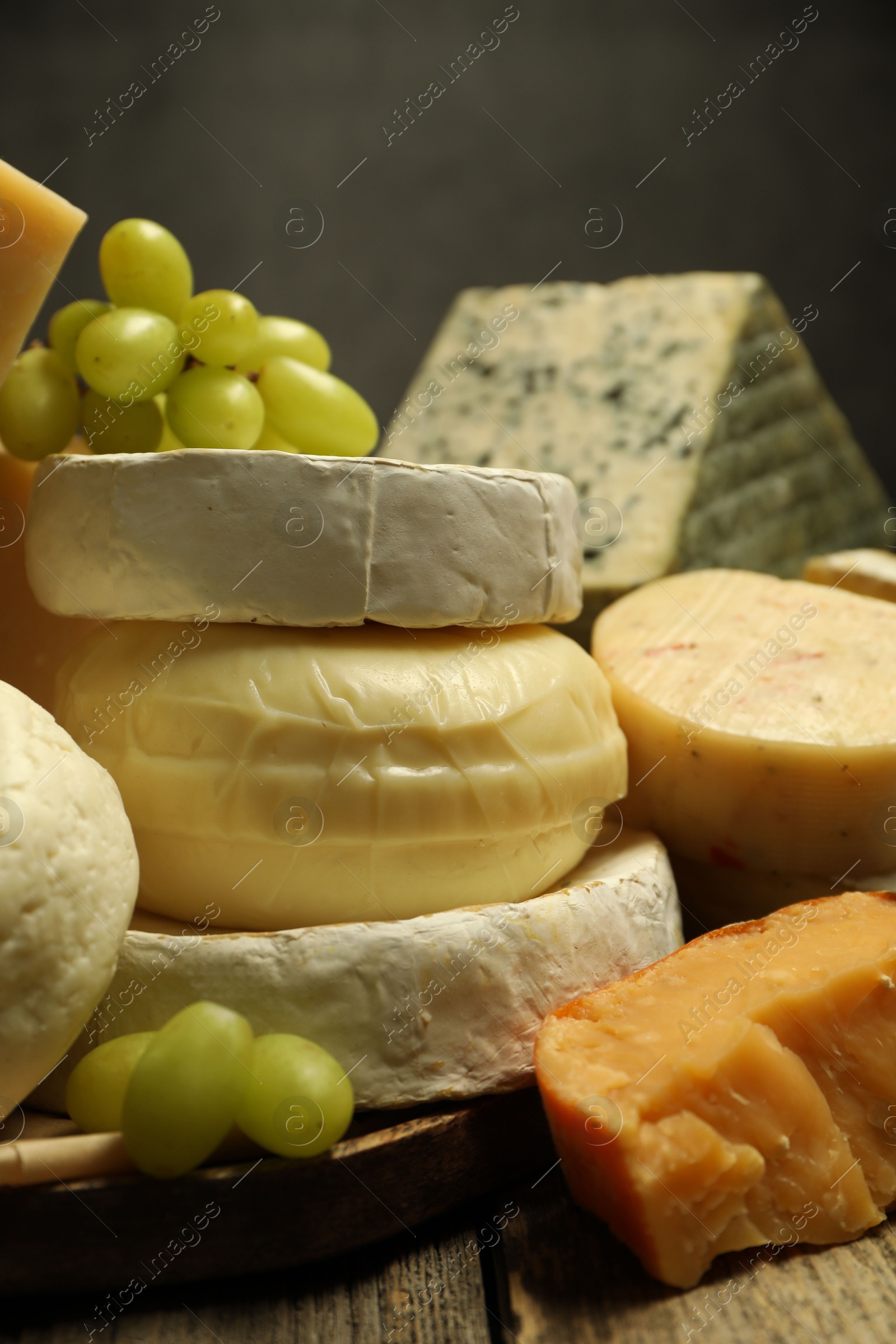 Photo of Different types of cheese and grapes on wooden table against dark background, closeup