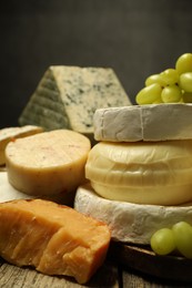 Photo of Different types of cheese and grapes on wooden table against dark background, closeup