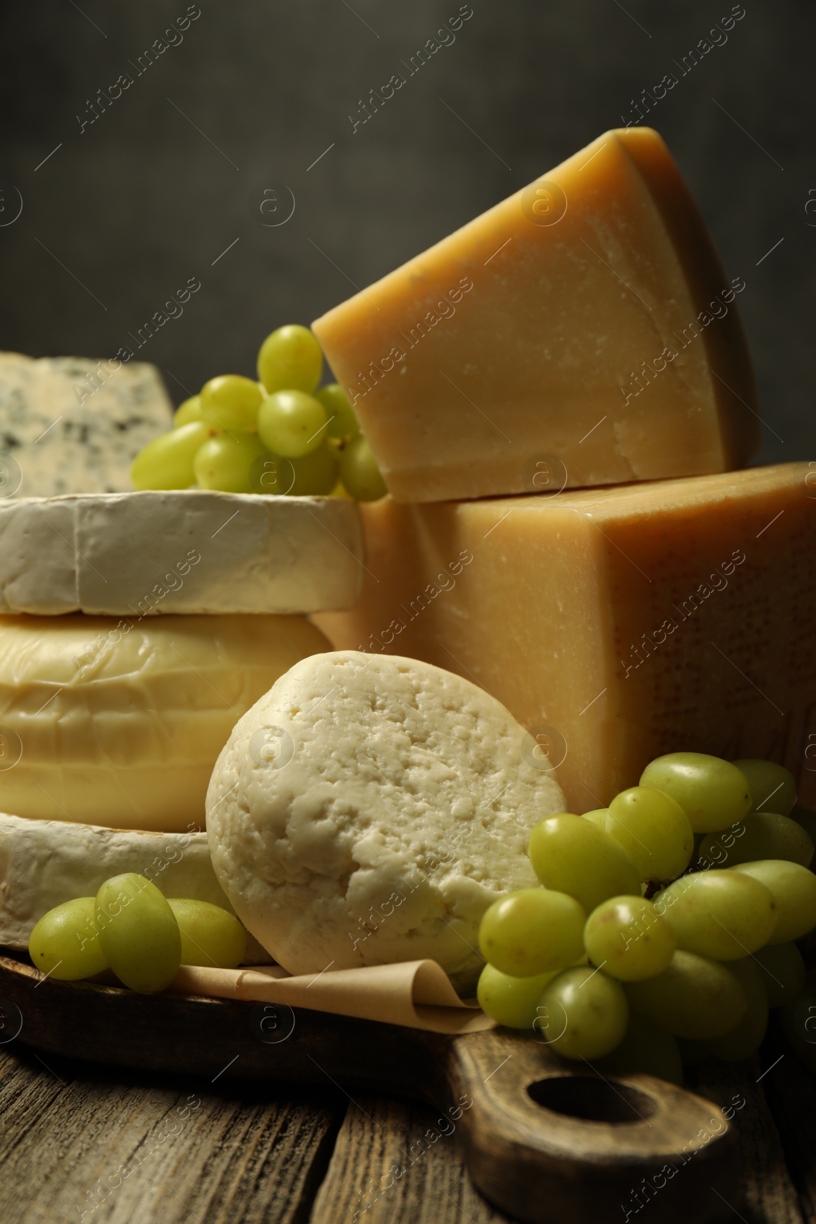 Photo of Different types of cheese and grapes on wooden table against dark background, closeup