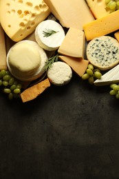 Photo of Different types of cheese, rosemary and grapes on dark textured table, flat lay. Space for text