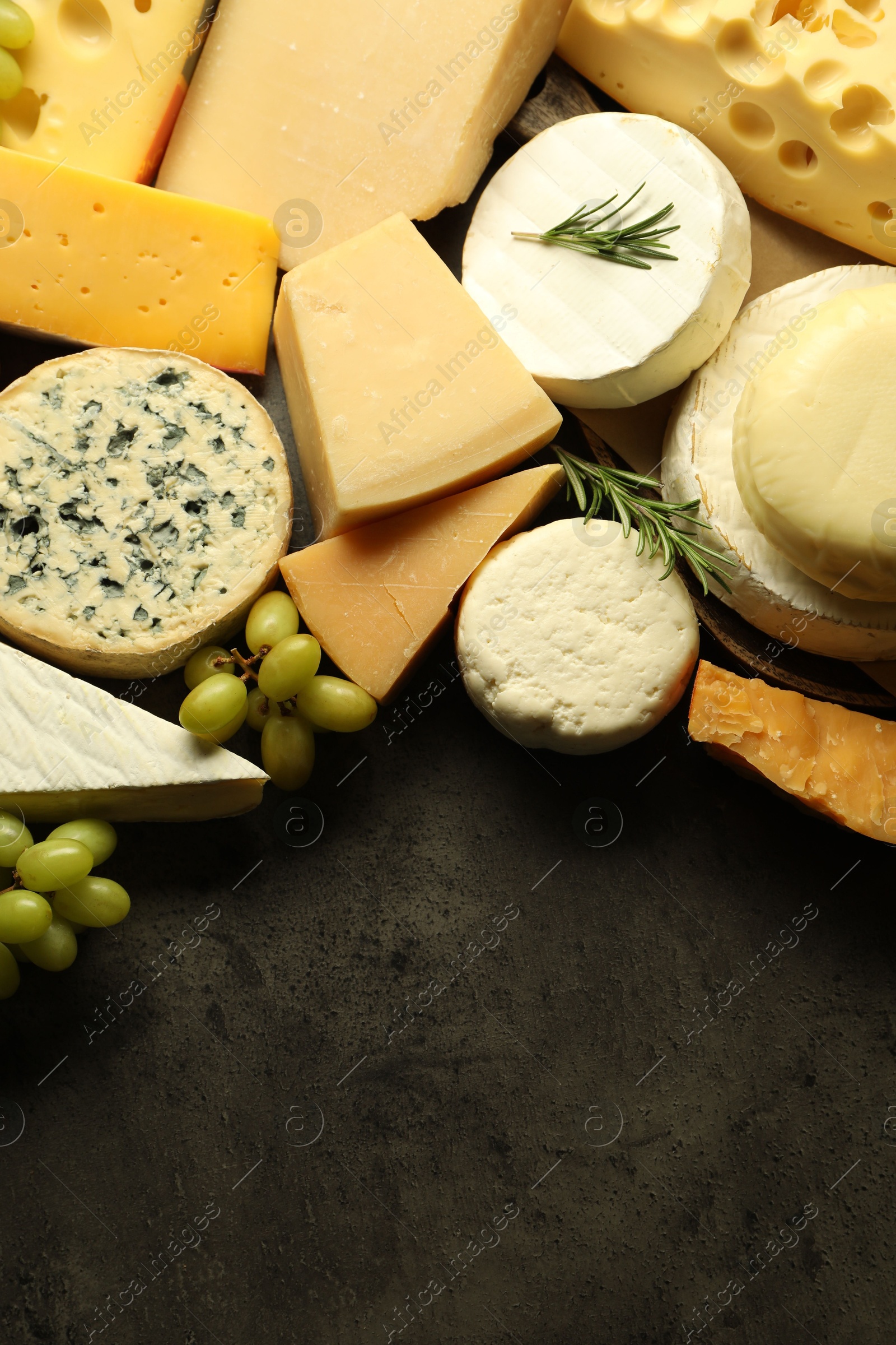 Photo of Different types of cheese, rosemary and grapes on dark textured table, flat lay. Space for text