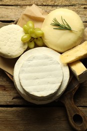 Photo of Different types of cheese, rosemary and grapes on wooden table, top view