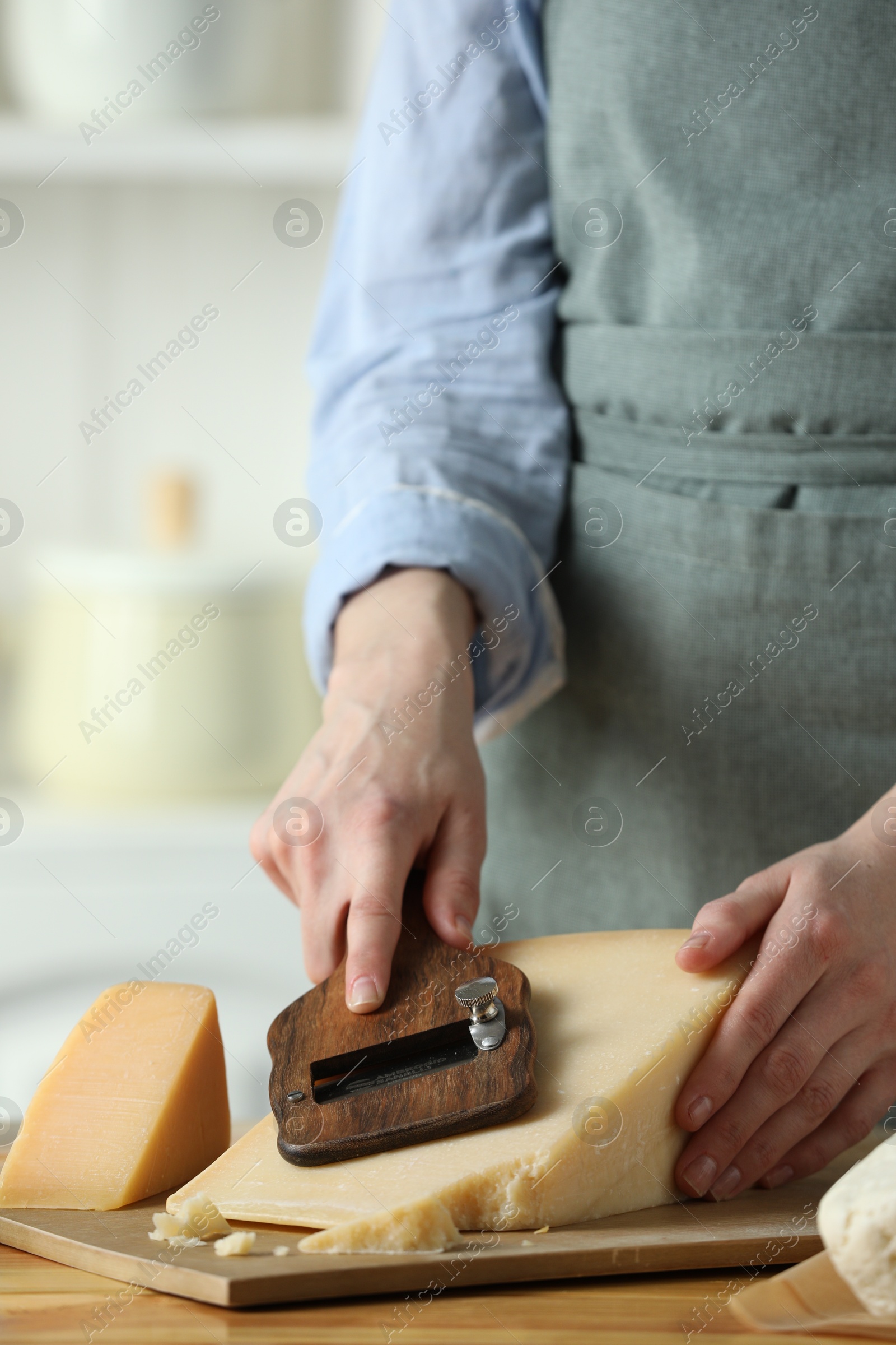 Photo of Woman cutting delicious cheese with slicer at wooden table indoors, closeup