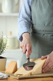 Photo of Woman cutting delicious cheese with slicer at wooden table indoors, closeup