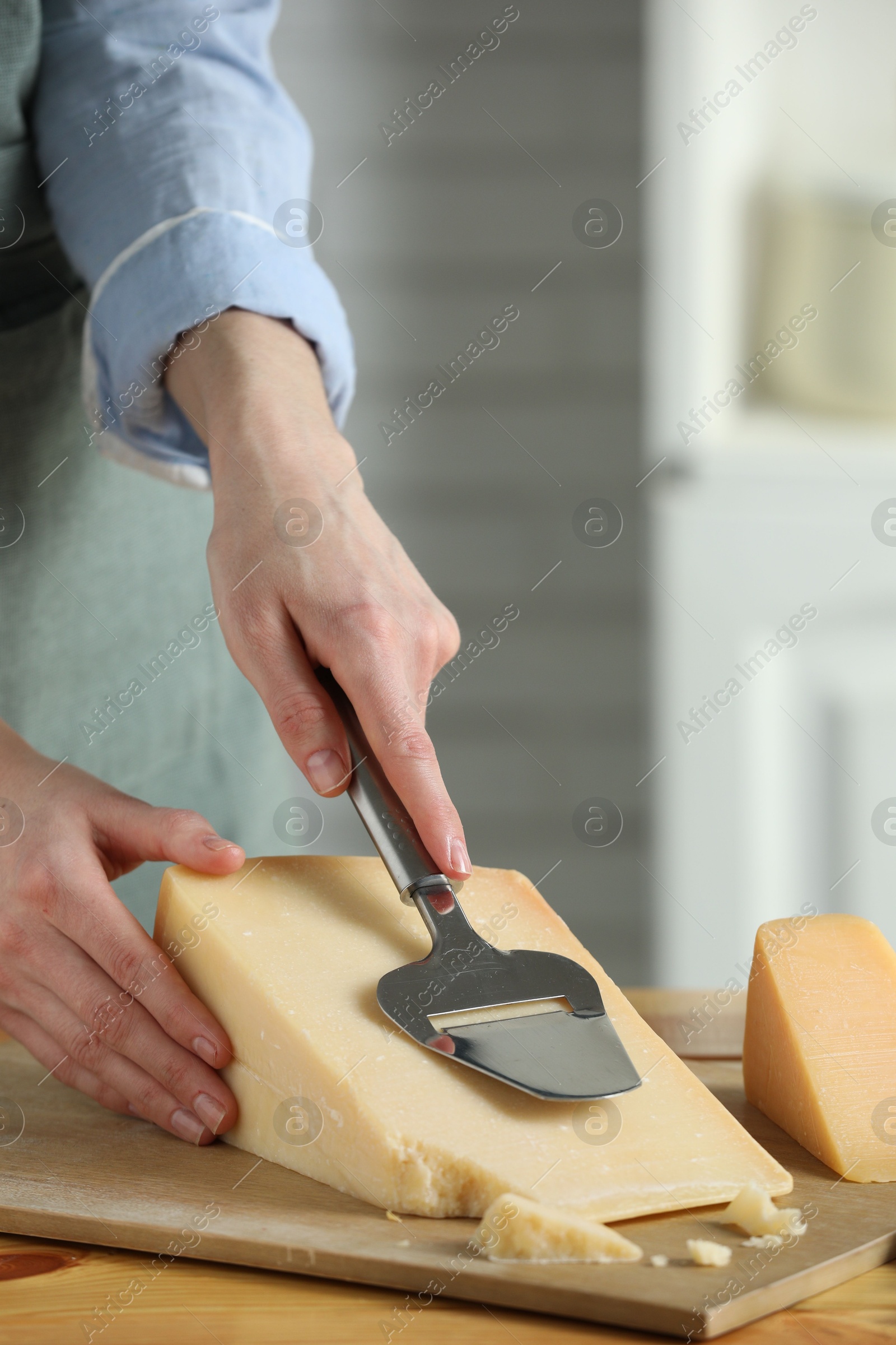 Photo of Woman cutting delicious cheese with slicer at wooden table indoors, closeup