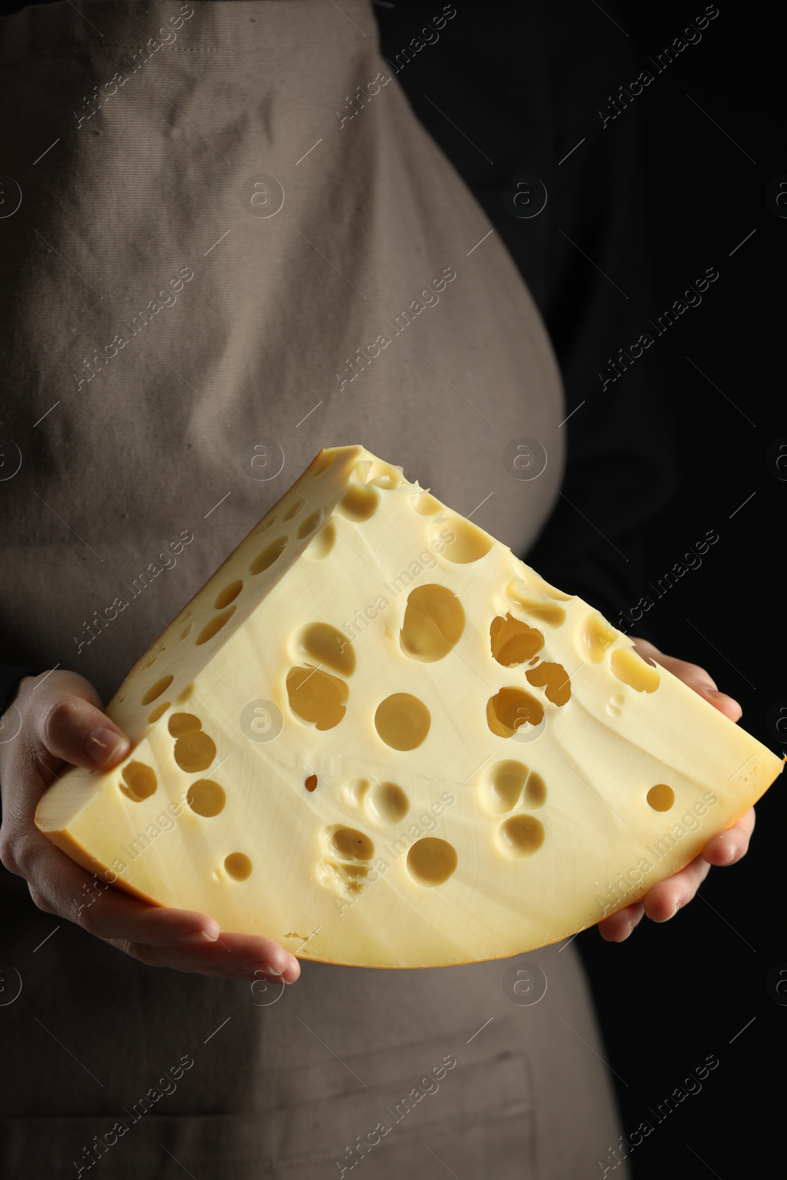 Photo of Woman with piece of delicious cheese on black background, closeup