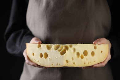 Photo of Woman with piece of delicious cheese on black background, closeup