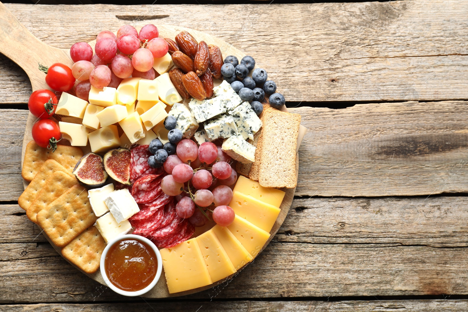 Photo of Different types of delicious cheese and other snacks on wooden table, top view. Space for text