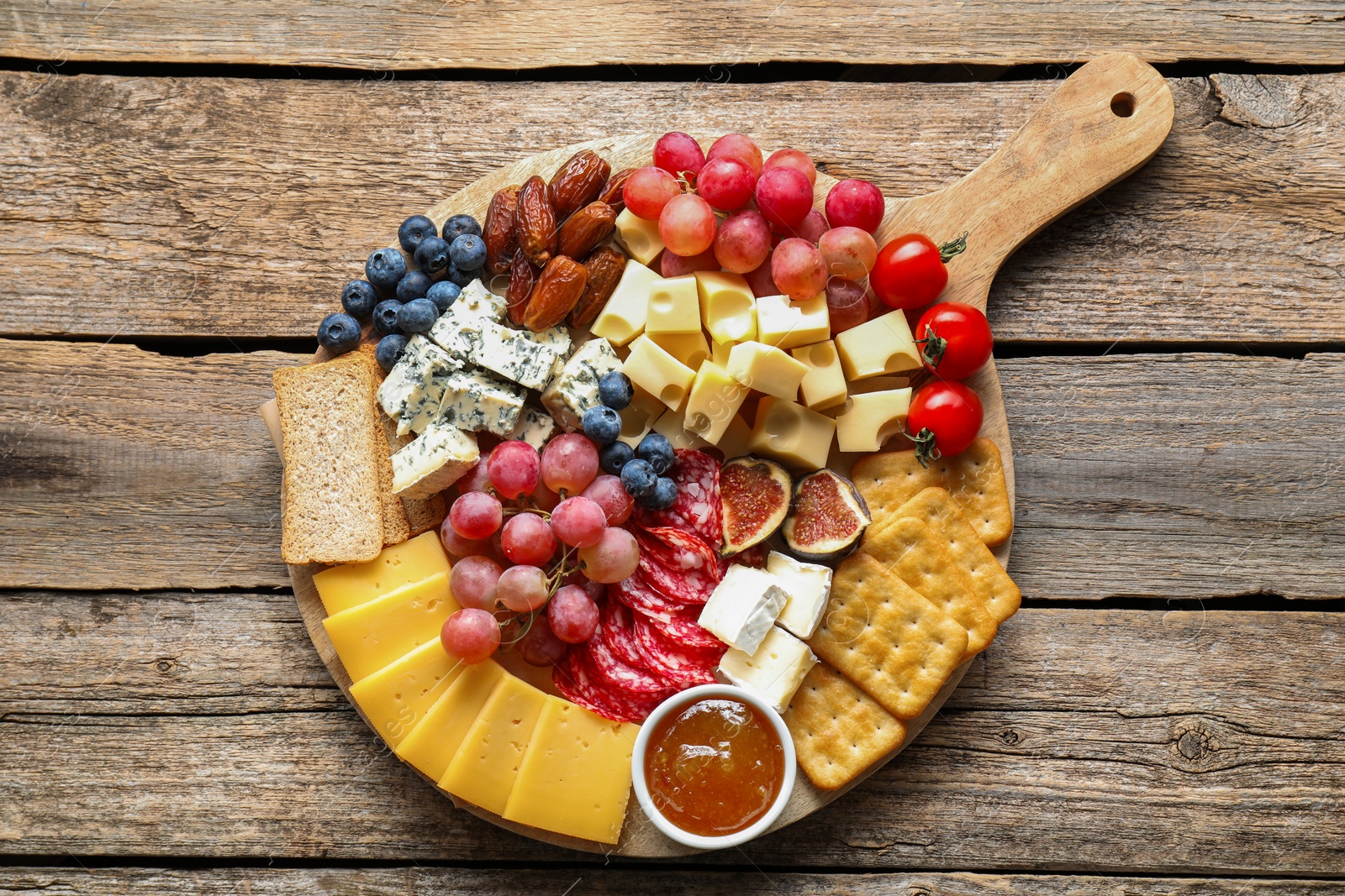 Photo of Different types of delicious cheese and other snacks on wooden table, top view