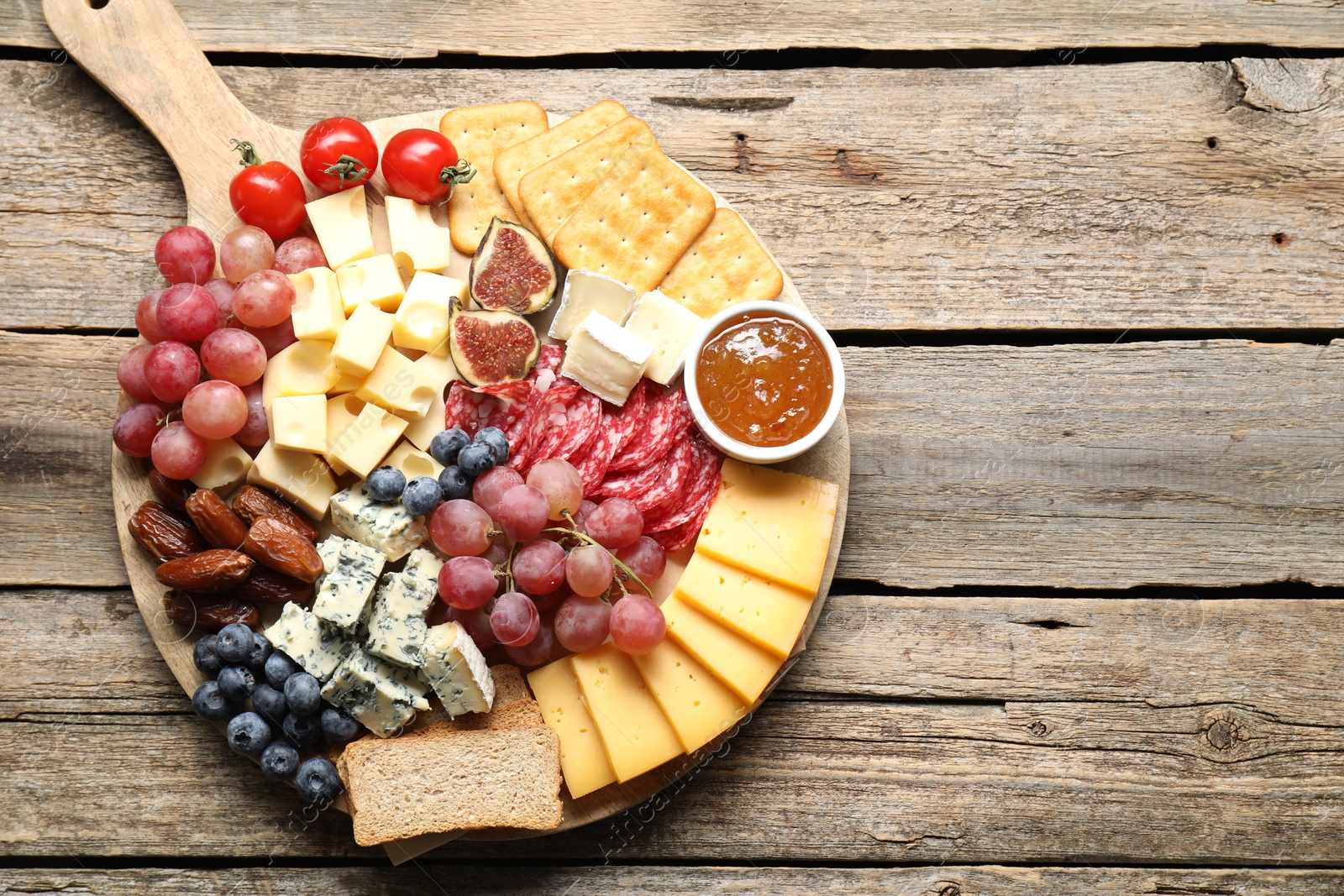 Photo of Different types of delicious cheese and other snacks on wooden table, top view. Space for text