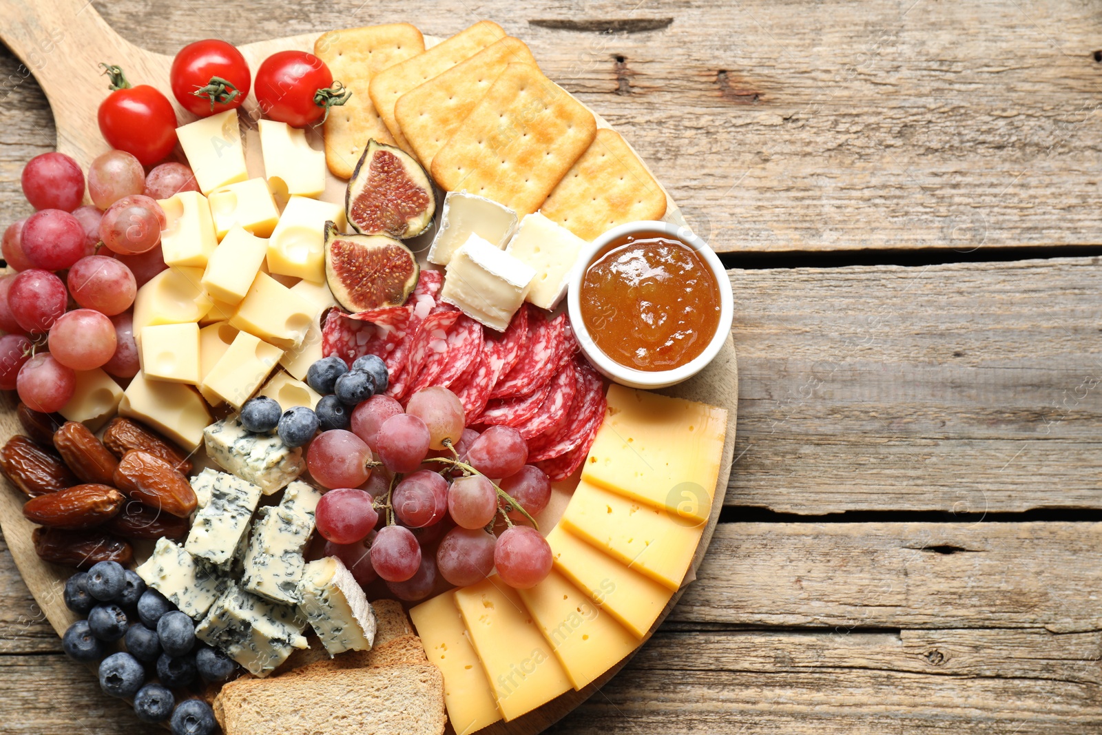 Photo of Different types of delicious cheese and other snacks on wooden table, top view. Space for text