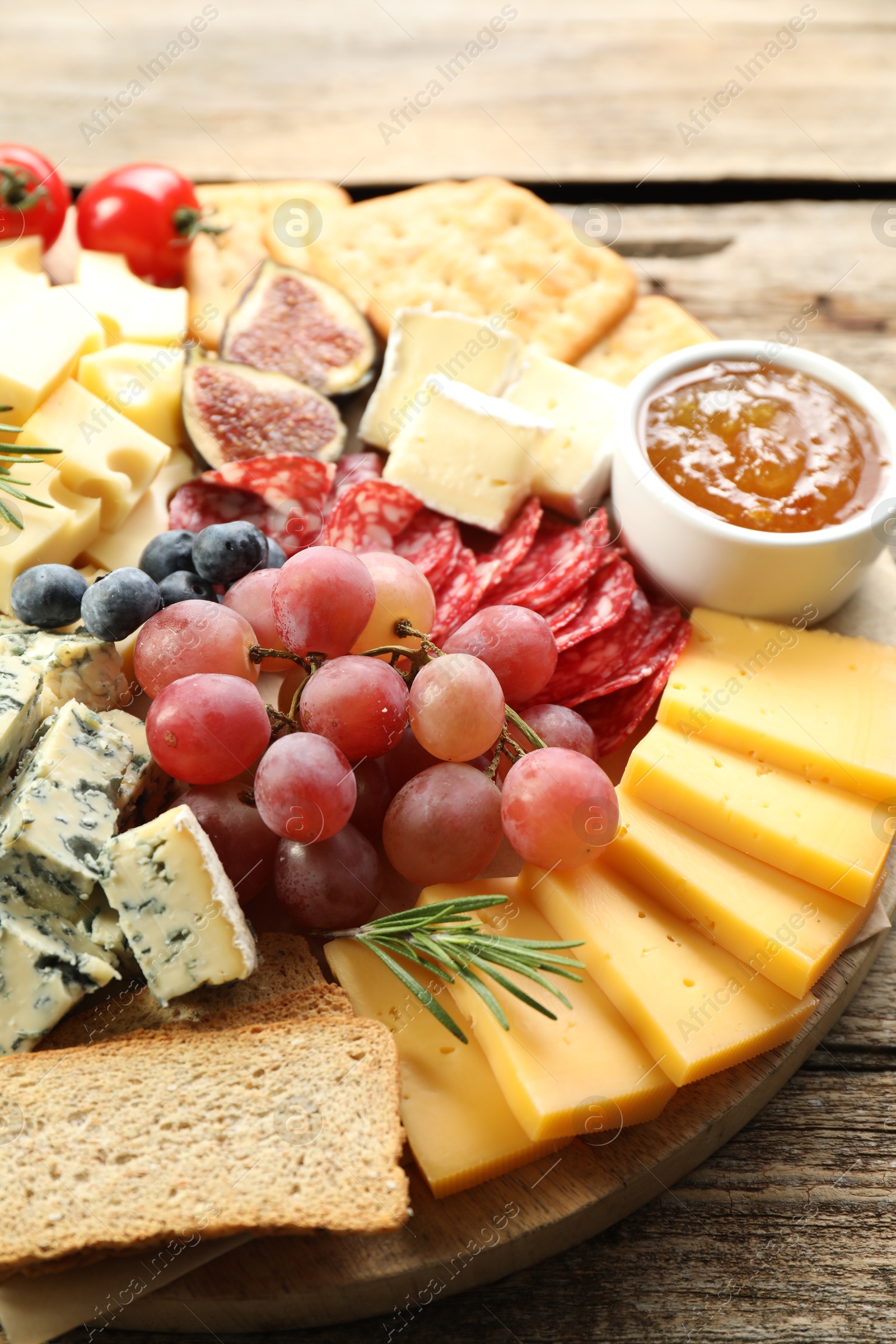 Photo of Different types of delicious cheese and other snacks on wooden table, closeup