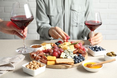 Photo of Women holding glasses of wine at light grey table with different snacks indoors, closeup