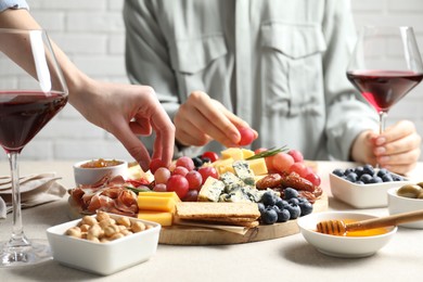 Photo of Women enjoying different snacks and wine during brunch at light grey table indoors, closeup