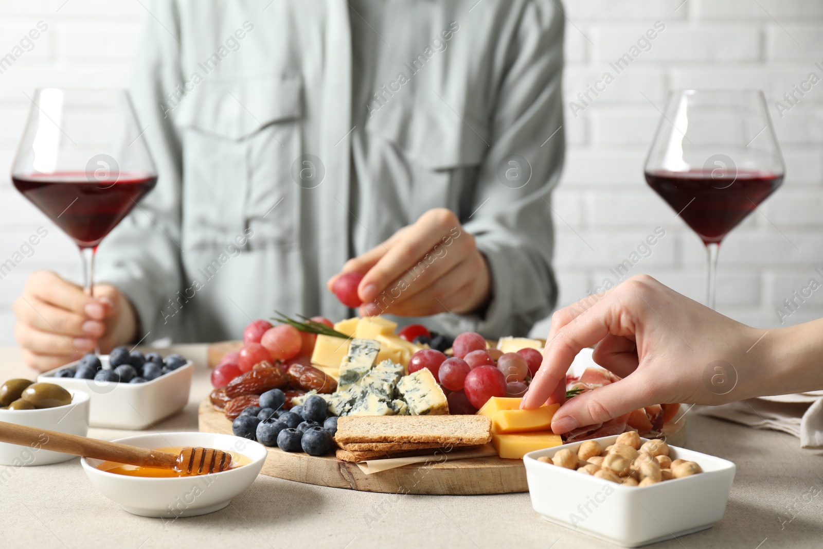 Photo of Women enjoying different snacks and wine during brunch at light grey table indoors, closeup