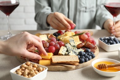 Photo of Women enjoying different snacks and wine during brunch at light grey table indoors, closeup